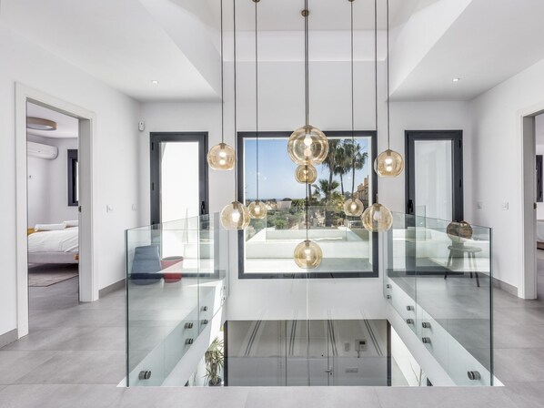 Un intérieur moderne avec une balustrade en verre, un lustre central et une vue sur l’extérieur.
