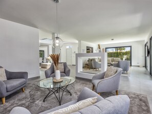 A modern living room with grey sofas, a glass coffee table, and a view of the outdoor seating area. - Villa Ruby | Pool - terrace - views (Sitio de Calahonda)