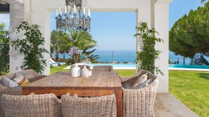 Un área de comedor al aire libre con mobiliario de mimbre, una mesa de madera y vistas al mar.