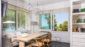 Un comedor moderno con una mesa y sillas de madera, un sofá y vista al océano.