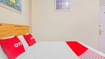 A hotel room with a wooden headboard, two red pillows, a white bedspread, a small window, and a white door.