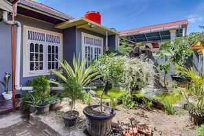 A courtyard with potted plants, a small pond, and a building with a red roof and white windows. - Hotel O New Bunga Sonsang Homestay Syariah (Padang)