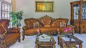 A spacious living room with a large brown sofa, ornate wooden chairs, and a glass coffee table. - Hotel O New Bunga Sonsang Homestay Syariah (Padang)