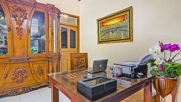 A wooden cabinet with glass doors, a framed picture on the wall, a desk with a laptop, printer, and potted orchid.