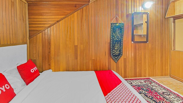 A room with wooden panel walls, a bed with red pillows, a hanging calligraphy piece, and a patterned rug. - Hotel O New Bunga Sonsang Homestay Syariah (Padang)