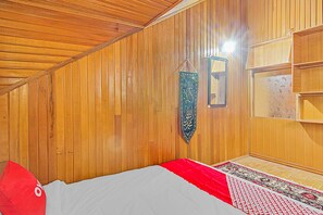 Habitació amb panells de fusta, un llit, un coixí vermell, una catifa de pregaria i un estendard de pregària penjant.