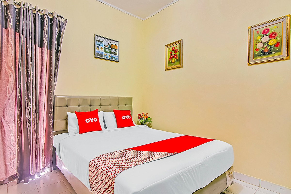 Una habitación de hotel con cama, cortinas, cabecero y dos cuadros en la pared.