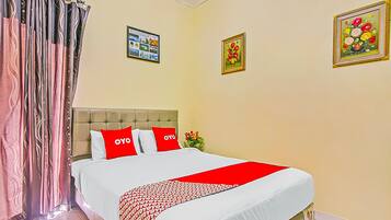 A hotel room with a bed, curtains, a headboard, and two framed pictures on the wall.