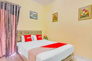 Una habitación de hotel con cama, cortinas, cabecero y dos cuadros en la pared.