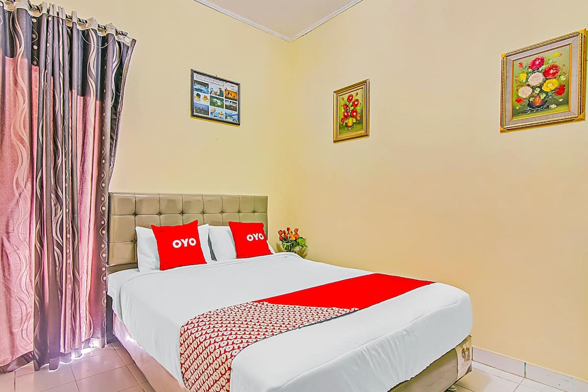 Une chambre d’hôtel avec un lit, des rideaux, une tête de lit et deux tableaux encadrés accrochés au mur.