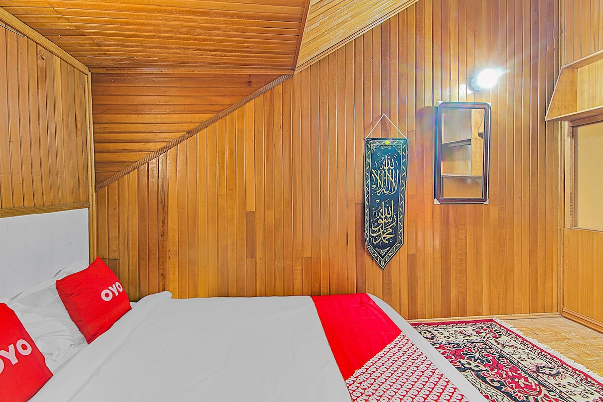 Ein Zimmer mit Holzwandverkleidung, einem Bett mit roten Kissen, einem hängenden Kalligraphie-Kunstwerk und einem gemusterten Teppich.