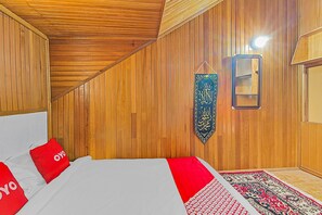 A room with wooden panel walls, a bed with red pillows, a hanging calligraphy piece, and a patterned rug. - Hotel O New Bunga Sonsang Homestay Syariah (Padang)