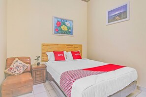 A bedroom with a wooden headboard, a bed with white bedding and red accents, a brown leather chair with a patterned pillow, a small nightstand with a plant, and two wall-mounted paintings. - Hotel O New Bunga Sonsang Homestay Syariah (Padang)