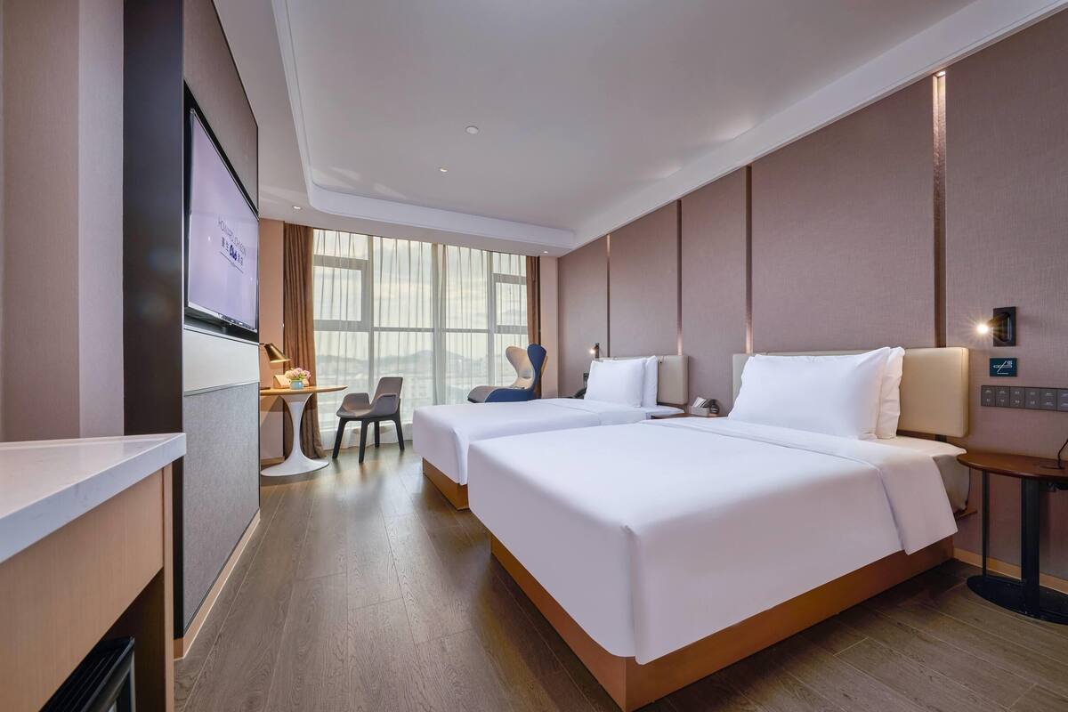 Une chambre d’hôtel avec deux lits, un bureau, une chaise, une télévision et une grande fenêtre.