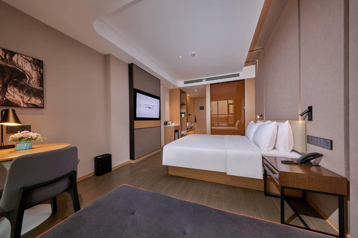 Une chambre d’hôtel moderne avec un grand lit, un bureau avec une chaise, une télévision et une petite table avec une lampe.