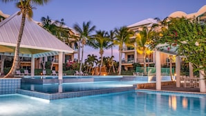 Ett poolområde på ett semesterhotell med flera nivåer av balkonger, palmer och solstolar.