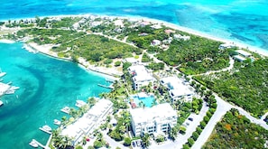 An aerial view of a coastal resort with multiple buildings, a marina with boats, and lush greenery.