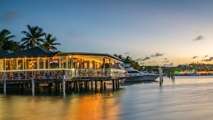 A waterfront building with a dock extending into calm water, featuring a glass facade and outdoor seating area. - YACHT CLUB D4 - Waters Edge Poolside Condo - Walk to Grace Bay Beach, Dining.   (The Bight Settlement)