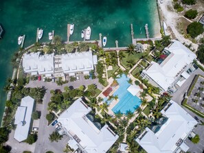 Une vue aérienne d’un complexe hôtelier comprenant plusieurs bâtiments, une piscine et des bateaux amarrés à un quai.
