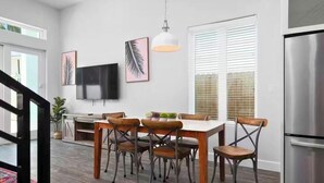 A modern kitchen with a dining area, stainless steel appliances, and a large window with blinds.
