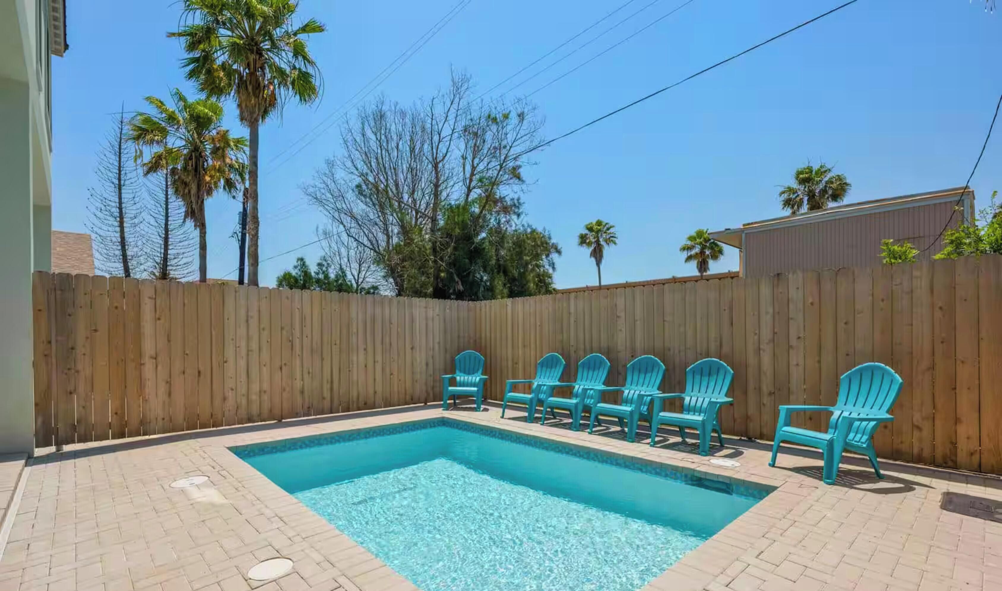 Une piscine rectangulaire entourée d’une clôture en bois et de chaises.