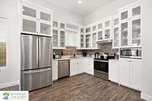 A modern kitchen with white cabinets, stainless steel appliances, and a wooden floor.