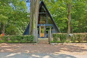 Ein Baumhaus mit Holztür und kleiner Veranda, umgeben von dichtem Grün.