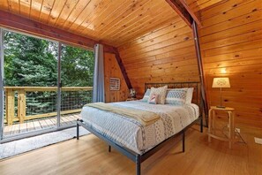 Ein Schlafzimmer mit Holzboden, einem Bett mit gemusterten Bettwaren, einem Nachttisch und Blick auf einen Balkon mit Holzgeländer.
