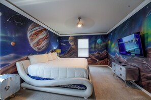 A bedroom with a space-themed mural, a bed, a dresser, and a television.