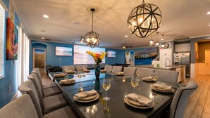 A modern dining room with a large table set for six, a ceiling fan, and a kitchen in the background. - Global Bowling Villa, 1GB wifi, video wall TV, private/heated pool, sleeps 34 (Davenport)