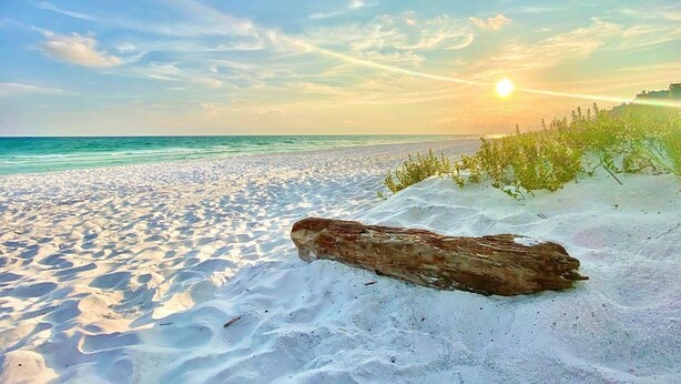 Una playa arenosa con una roca grande en primer plano y una puesta de sol al fondo.