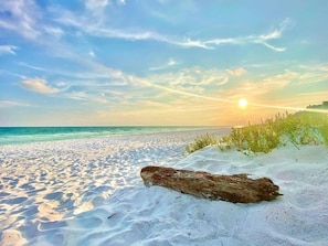 Une plage de sable avec un grand rocher au premier plan et un coucher de soleil en arrière-plan.
