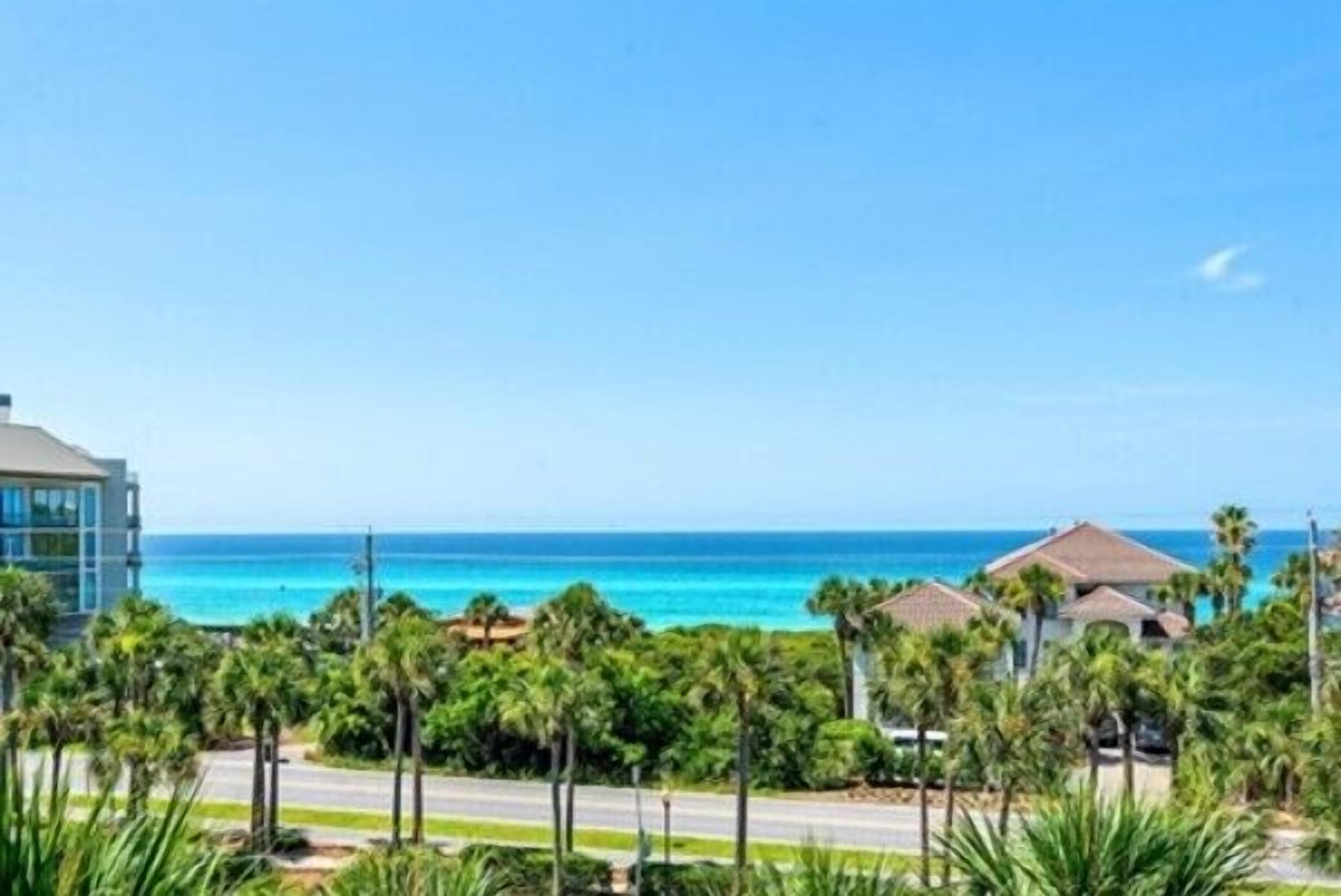 A coastal view with a modern building, palm trees, and a clear blue sky.