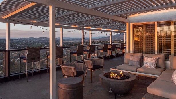 A covered outdoor seating area with chairs and a sofa, a fire pit, and a view of the cityscape.