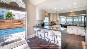 A modern kitchen with a large island, bar stools, and a view of a swimming pool.