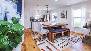 Une cuisine moderne avec des meubles blancs, une table à manger en bois et une grande plante.