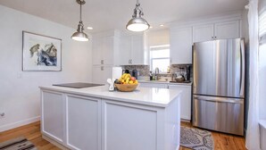 Une cuisine moderne avec des meubles blancs, un réfrigérateur en acier inoxydable et des luminaires suspendus.