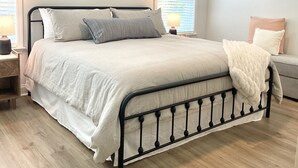 Un dormitorio con cama, ventilador de techo, mesita de noche, lámpara y ventana con persianas.