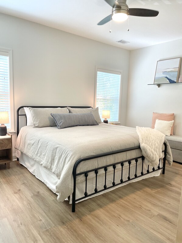 A bedroom with a bed, a ceiling fan, a nightstand, a lamp, and a window with blinds.