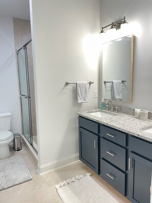 Un baño moderno con cabina de ducha de vidrio, inodoro blanco, lavamanos con encimera de mármol y armarios oscuros.