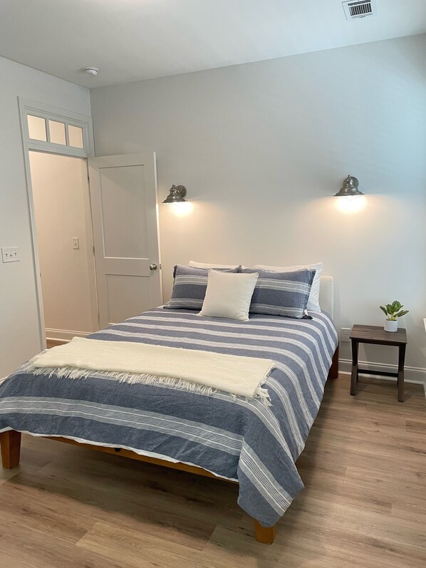 A bedroom with a bed, bedside lamps, a small table with a plant, and a door.