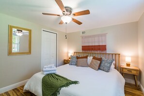 Une chambre à coucher bien rangée, avec un lit, un ventilateur de plafond, des lampes de chevet et un miroir au mur.