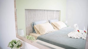 Ein ordentlich eingerichtetes Hotelzimmer mit Bett, Kissen, einem Nachttisch, einer Lampe und einer kleinen Topfpflanze.