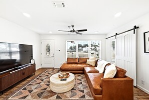 Uma sala de estar moderna com um sofá seccional, uma televisão de tela plana, um ventilador de teto e um tapete estampado.