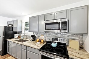 A modern kitchen with grey cabinets, a stainless steel microwave, a black stove, and a granite countertop.
