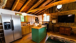 Una cucina rustica con travi in legno, un frigorifero in acciaio inox, pensili e basi in legno, un'isola centrale e un televisore a schermo piatto.