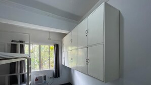 Um quarto de dormitório com beliches, uma janela com cortinas e um guarda-roupa branco.