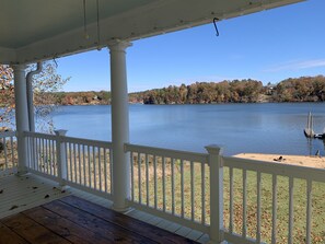 A covered porch with white railings overlooking a lake, with trees and a distant house visible. - Beautiful lakefront home W/Breathtaking view (Claremont)