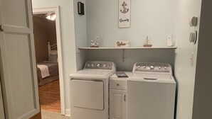 A laundry room with two white washing machines and a shelf with decorative items.