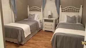 A bedroom with two beds, a nightstand with a lamp, and a window with curtains.